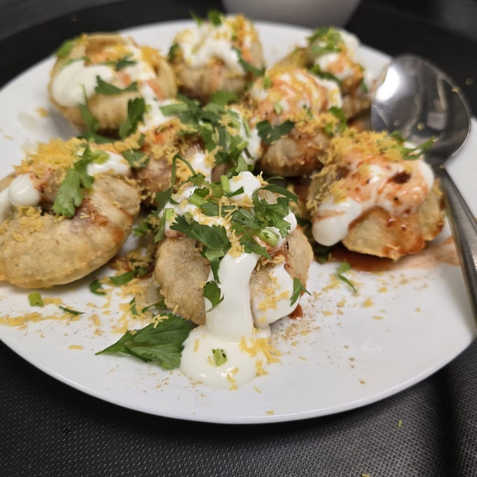 Crisp chaat topped with yogurt, chutney, sev, and cilantro.